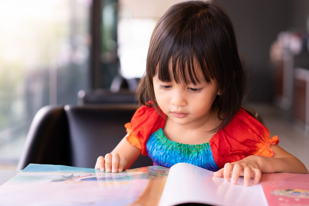 Little girl in a preschool sits and practices reading comprehension, which is essential to the Nevada Ready grant program.